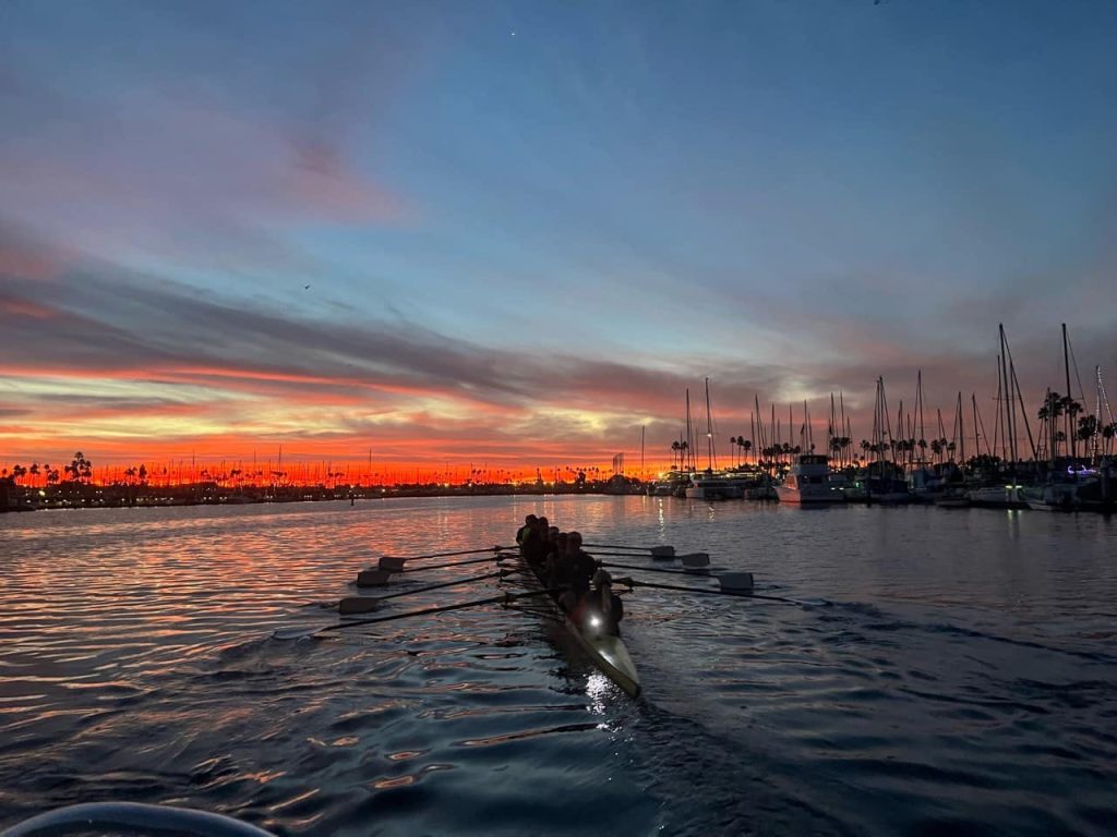Silhouette of rowing eight heading into sunrise in a marina