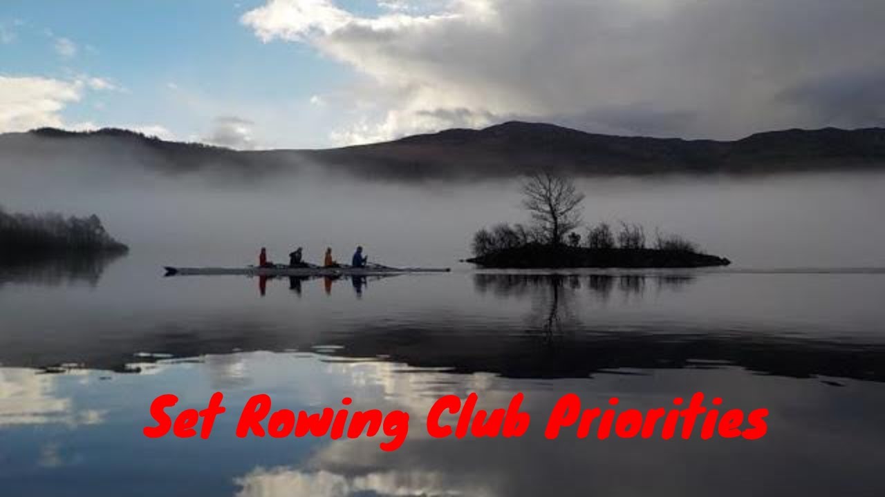 silhouette rowing four on a still lake with misty background, island with a prominent tree.