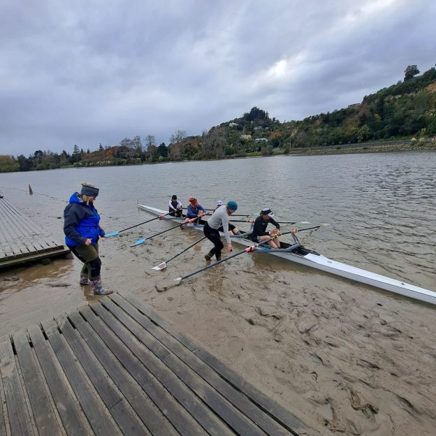 Quad scull rowing boat beach launching into muddy river in Whanganui New Zealand