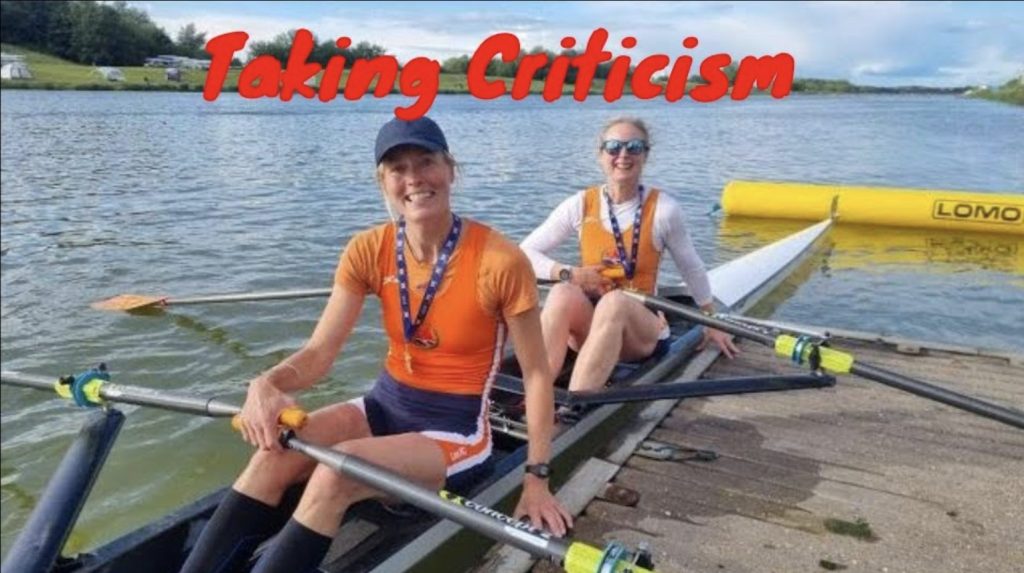 Two women in a rowing boat wearing orange uniforms with medals.