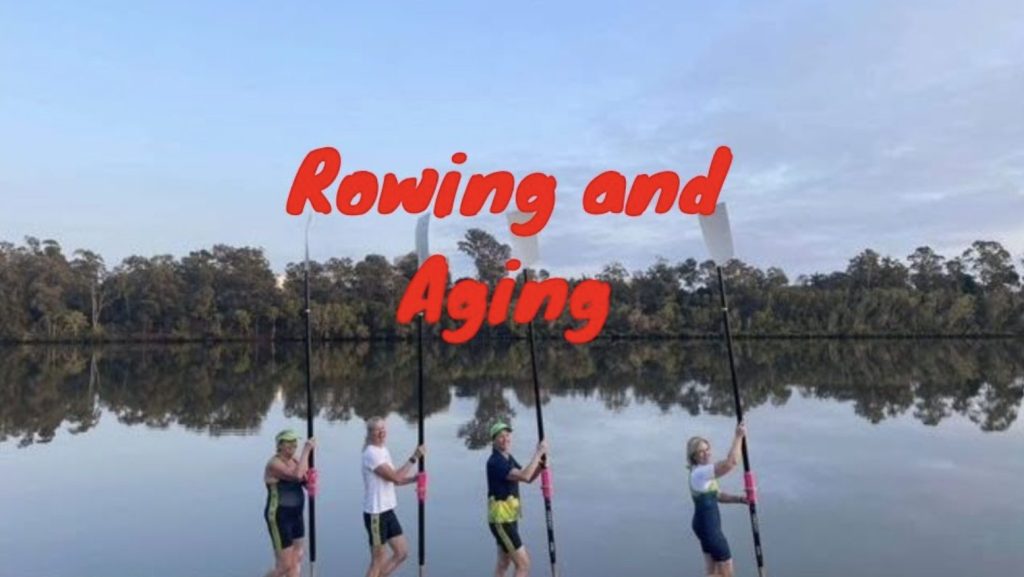 four women carrying oars beside a river smiling.