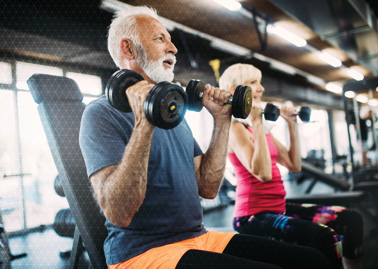 Two older athletes in a gym lifting hand weights