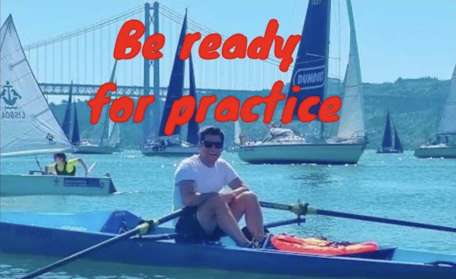 smiling man in a coastal rowing single scull with two sailing boats behind